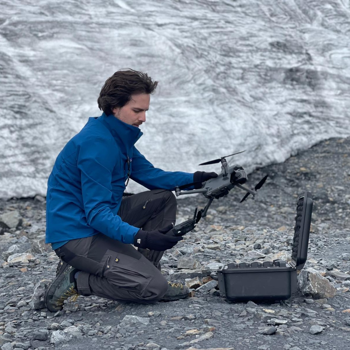 Dr Olly Bartlett preparing a survey drone on glacial moraine in front of a glacier